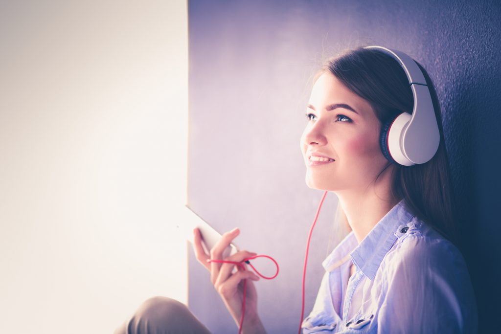 Woman listening music in headphones on windowsill background.